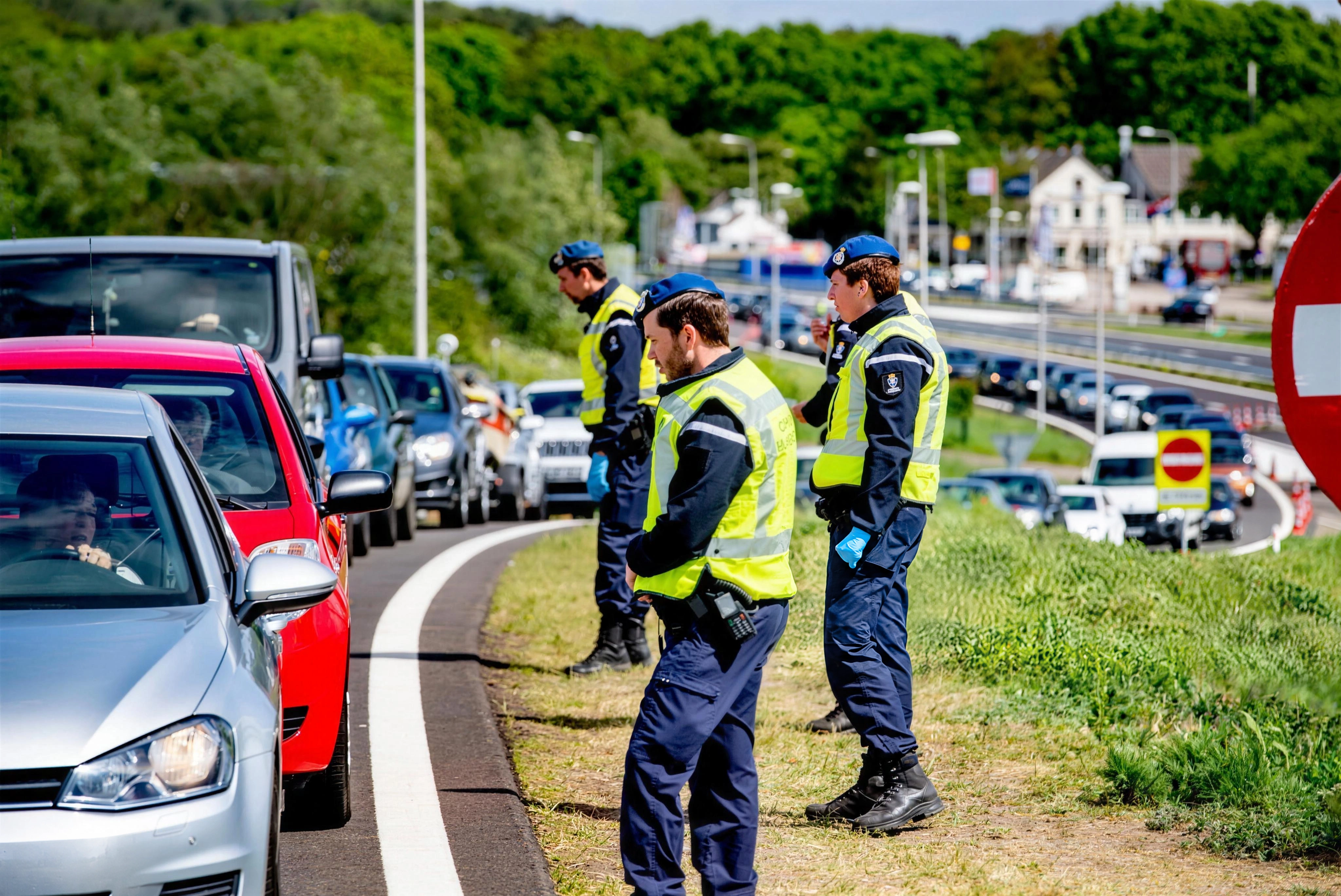 Drie medewerkers van de Koninklijke Marechaussee langs een rij voertuigen